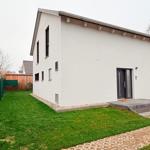 Moderne Villa mit Garten und Terrasse. Schwarze Fenster und Tür. Grasfläche und Kiesweg.