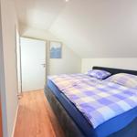 Schlafzimmer mit Doppelbett, Holzboden und schräger Decke. Tür und Wandbild sind sichtbar.