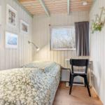 Bedroom with bed, desk, and window. Walls made of wood, pictures on the wall.