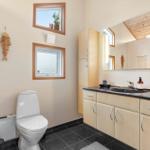 Bathroom with toilet, sink, and two windows. Wooden furniture and mirror.