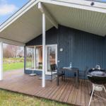 Deck with table, chairs, and grill in front of blue wooden house with glass doors.