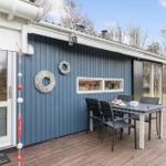 Deck with table and chairs in front of blue house with windows and decor.