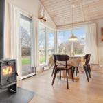 Room with stove, dining table, and large windows. Wooden ceiling and floor.