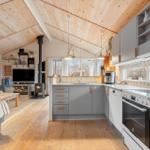 Kitchen with gray cabinets and wood ceiling. Living area with fireplace and TV.