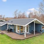 A blue holiday home with wooden terrace, grill and garden. Large windows and gable roof.