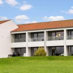 Modern holiday home with balconies and red tiled roof on green lawn.