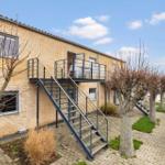 A two-story house with balcony and metal stairs. Trees and paved paths.