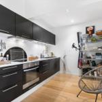 Kitchen with black cabinets, wooden floor, and metal shelf. A round seating area is in the room.