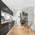 Kitchen with black cabinets and wooden floor. Metal shelf and chair in the background.