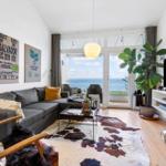 Living room with sofa, TV, and ocean view through glass door.