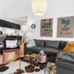 Living area with sofa, coffee table, and kitchen. Wall decor and wooden floor.