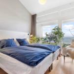 Bedroom with bed, sea view through windows, and plants