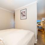 Schlafzimmer mit Bett und Bild an der Wand. Durchgang zu Wohnbereich mit Fernseher.