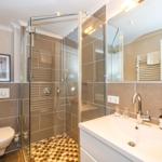 Badezimmer mit Dusche, Waschbecken und Toilette. Fliesenwand und Spiegel.