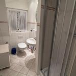 Badezimmer mit Dusche, Waschbecken und Toilette. Fenster mit Vorhängen.