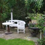 Weißer Sitzbereich mit Tisch auf Steinplatten im Garten mit Pflanzen und Beleuchtung.