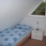 Ein Schlafzimmer mit Dachschrägen, Bett mit blauem Bettzeug und Nachttisch mit Lampe.