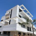 Modern white building with balconies and glass railings under blue sky.