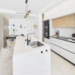 Modern kitchen with island, stainless steel sink, and white cabinets. Dining area in background.