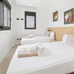 Two beds with white linens and towels. Wood headboard and two windows.