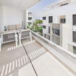 Terrace with seating and glass railing. View of modern buildings and green areas.