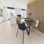 Dining area with round table and chairs next to wood panel. Kitchen and living area are open.