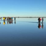 Menschen gehen auf einer eisbedeckten Fläche. Im Hintergrund sind Windräder sichtbar.