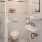 Badezimmer mit Toilette, Waschbecken und Spiegel. Wandbild zeigt Strandmotiv.