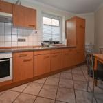 Küche mit Holzschränken, Spüle und Esstisch mit Stühlen.