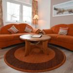 Ein Wohnzimmer mit zwei orangefarbenen Sofas, einem runden Holztisch und einem runden Teppich.