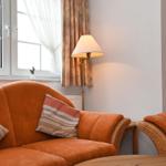 Ein Wohnzimmer mit orangefarbenem Sofa, Stehlampe und Fenster mit Vorhängen.