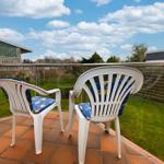 Terrasse mit zwei weißen Stühlen und blauen Sitzkissen. Blick auf grünen Garten und Himmel.