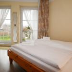 Schlafzimmer mit Doppelbett, zwei Fenstern und Blick auf Balkon.