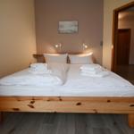 Ein Bett mit weißer Bettwäsche und gefalteten Handtüchern. Holzrahmen und Wandbilder.