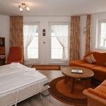 Schlafzimmer mit Bett, Sofa, Fernseher und Fenstern mit Vorhängen.