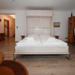 Schlafzimmer mit Bett, Fernseher und Holzmöbel. Durchgang zur Badewanne.