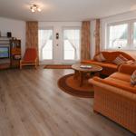 Wohnzimmer mit orangefarbenen Sofas, Holzboden und Fernseher.