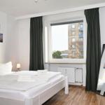 Schlafzimmer mit weißem Bett, Fenster mit Blick auf Gebäude und dunklen Vorhängen.