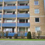Wohnhaus mit blauen Balkonen und Fenstern. Grünflächen und gepflasterte Straße.