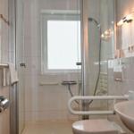 Badezimmer mit Dusche, WC und Waschbecken. Fenster, Handtuchhalter und Heizung sind sichtbar.