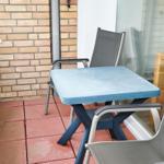 Terrasse mit Tisch und zwei Stühlen, rote Fliesen und Backsteinmauer.