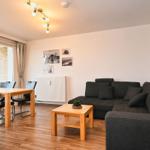 Wohn- und Essbereich mit Sofa, Tisch und Stühlen. Fenster mit Blick auf Gebäude.