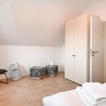 Schlafzimmer mit Bett, Kleiderschrank und Stuhl. Durchgang zur Badewanne.