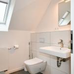 Badezimmer mit Toilette, Waschbecken und Dachfenster. Wandfliesen und Spiegel.