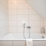 Dusche mit Handbrause und Badewanne in weißer Fliesenwand.