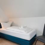 Ein Schlafzimmer mit Dachschrägen, Bett, Stuhl und Nachttisch.