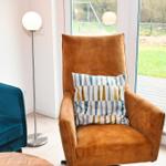 Ein braunes Sessel mit Kissen steht vor einem Fenster mit Blick auf einen Garten.