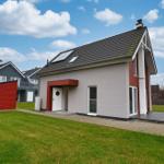 Moderne Villa mit rotem Anbau, Garten und Terrasse unter blauem Himmel.