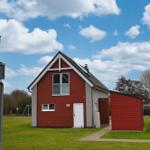 Rotes Haus mit weißer Tür und Terrasse auf grünem Grund.