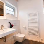 Badezimmer mit Waschbecken, Toilette und Heizkörper. Nebenraum mit Holzsauna.